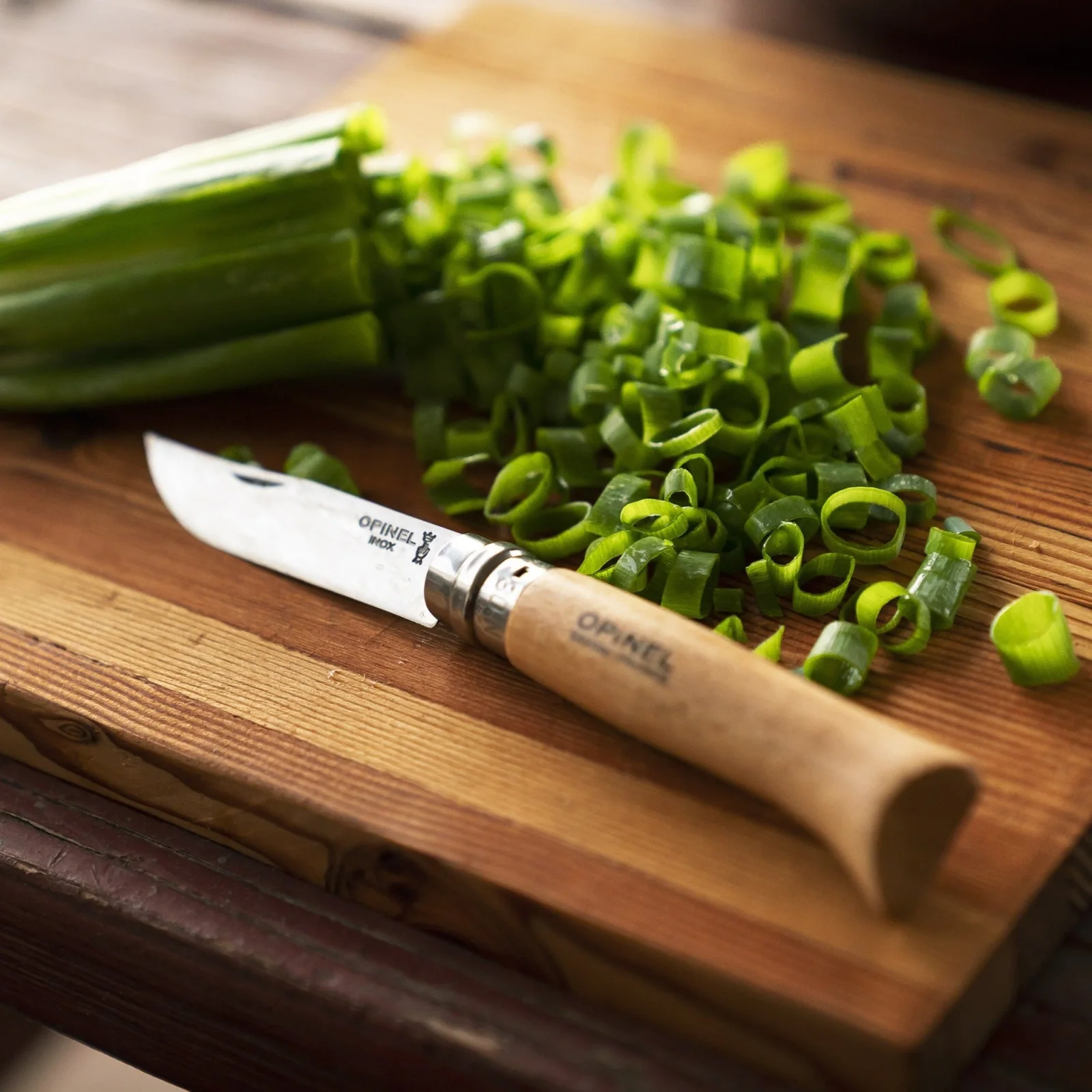 A knife and scallions on a cutting board