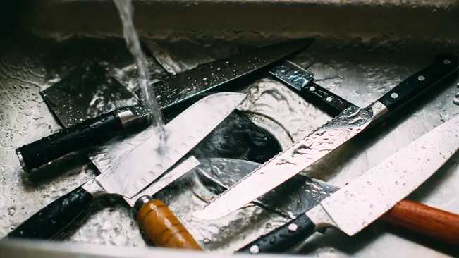 Several knives being washed in a sink