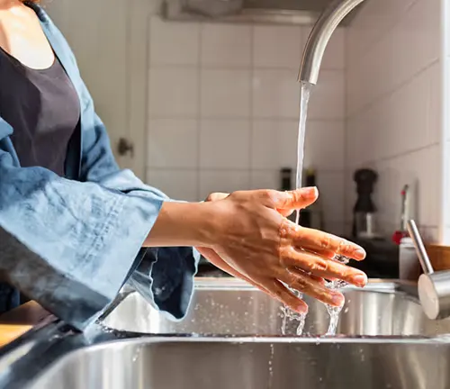 Person washing hands with soap under running water at a kitchen sink