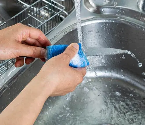 Hands carefully scrubbing a knife with a blue sponge under running water in a sink