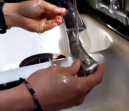 Hands washing a knife under a tap