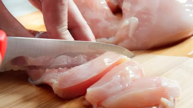 knife slicing through raw chicken on a cutting board