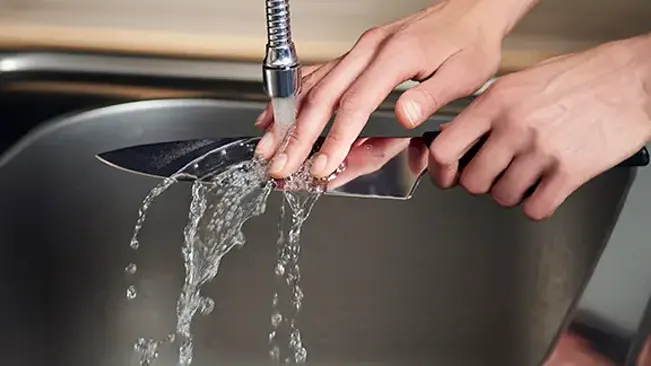 Hands washing a chef's knife under running tap water