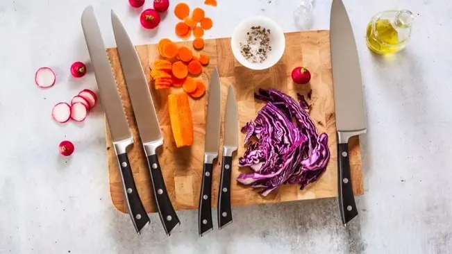 Assorted knives on a countertop with sliced vegetables