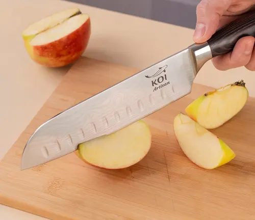 Hand holding a Koi Artisan Santoku knife, slicing an apple on a wooden cutting board