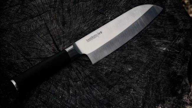 Sharp Santoku knife with a black handle resting on a dark, textured wooden surface