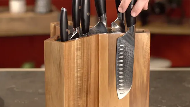 Hand pulling a Santoku knife from a wooden knife block on a kitchen countertop