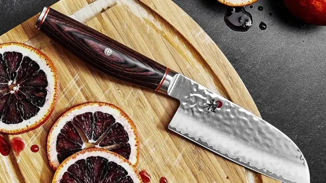 Santoku knife with a decorative design on a cutting board, surrounded by sliced blood oranges