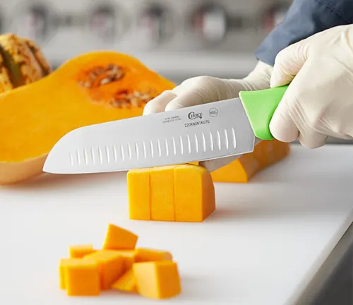 Person wearing gloves dicing a butternut squash with a Santoku knife on a white cutting board