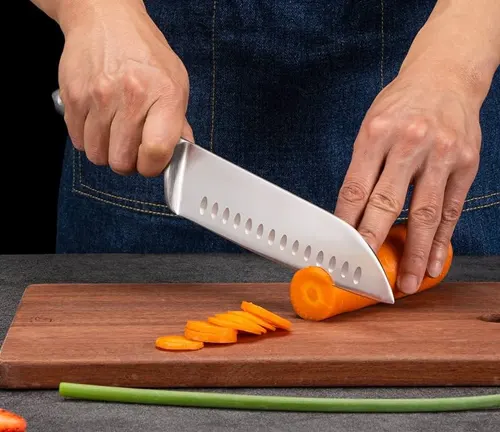 Person skillfully slicing a carrot with a Santoku knife on a wooden cutting board